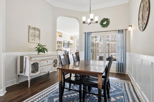 dining area with arched walkways, a wainscoted wall, crown molding, and wood finished floors