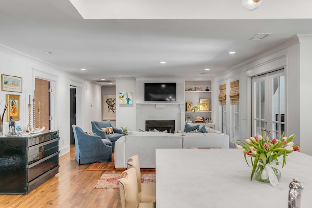 interior space with built in shelves, wood finished floors, visible vents, a fireplace, and crown molding