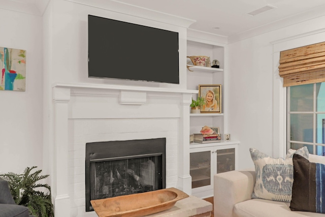 living area with visible vents, built in shelves, a brick fireplace, and ornamental molding