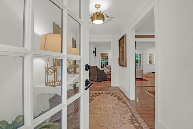 corridor featuring french doors, wood finished floors, baseboards, and ornamental molding