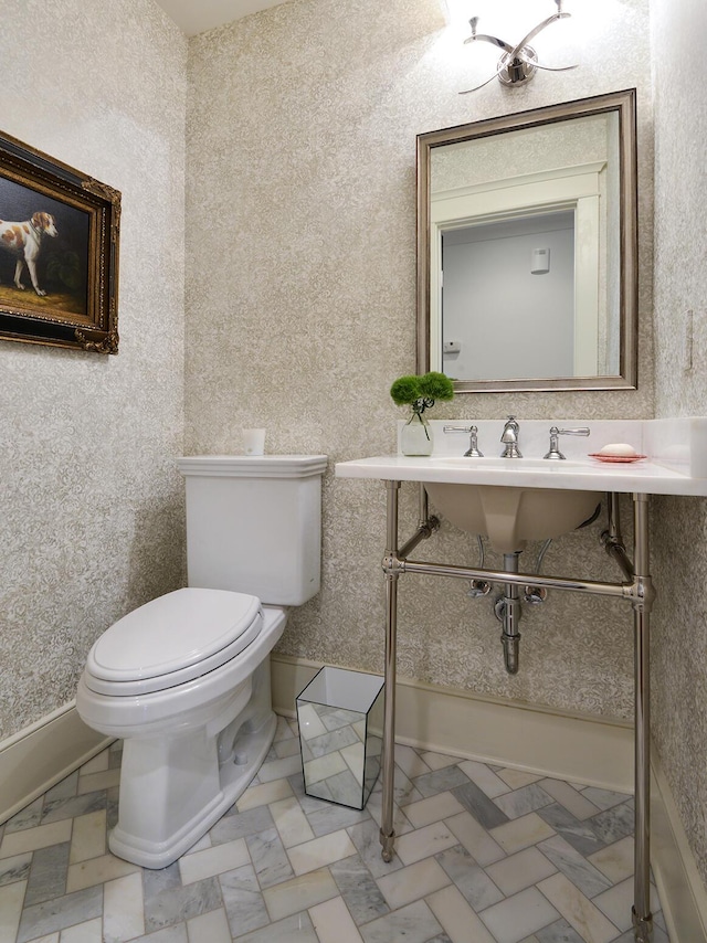 bathroom with wallpapered walls, toilet, baseboards, and a sink