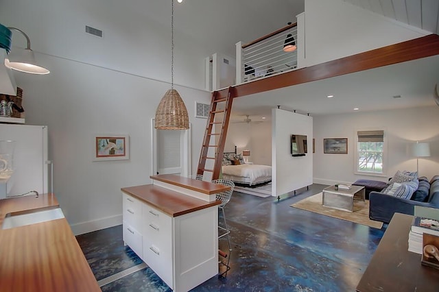 kitchen featuring visible vents, concrete flooring, freestanding refrigerator, a towering ceiling, and white cabinetry