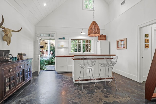 kitchen featuring visible vents, freestanding refrigerator, concrete floors, white cabinets, and hanging light fixtures