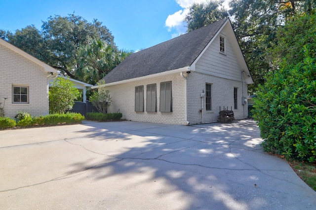 view of side of home with concrete driveway, brick siding, and roof with shingles