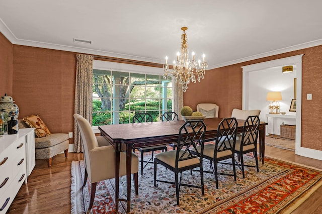 dining room featuring a notable chandelier, visible vents, crown molding, and wood finished floors