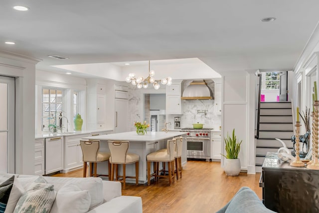 kitchen with light countertops, premium range, white cabinetry, wall chimney exhaust hood, and a sink