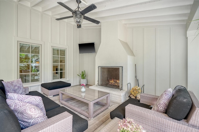 living room with a ceiling fan, wood finished floors, beamed ceiling, a fireplace, and a decorative wall