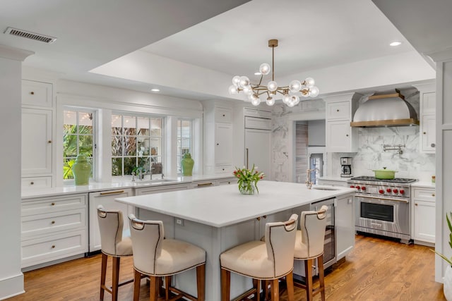 kitchen with visible vents, beverage cooler, a sink, designer stove, and wall chimney range hood