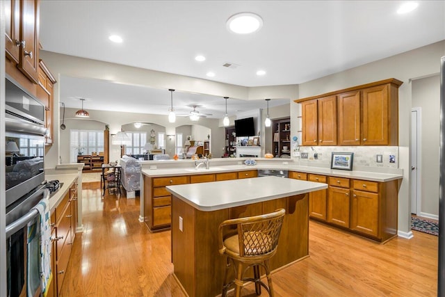 kitchen with ceiling fan, backsplash, kitchen peninsula, a kitchen bar, and light wood-type flooring