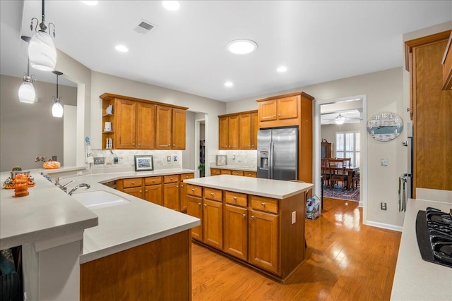 kitchen with kitchen peninsula, stainless steel refrigerator with ice dispenser, sink, light hardwood / wood-style flooring, and hanging light fixtures