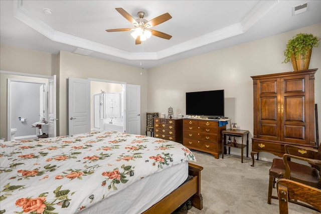 carpeted bedroom featuring a tray ceiling, connected bathroom, ceiling fan, and crown molding