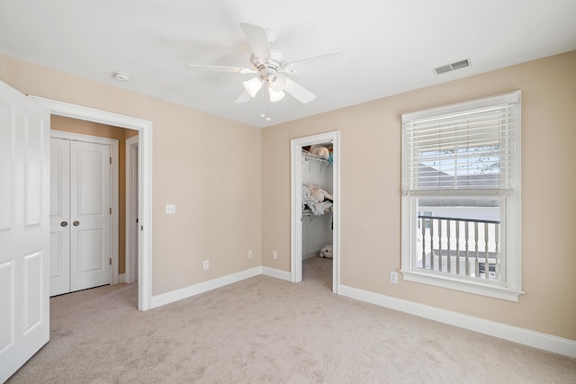 unfurnished bedroom featuring ceiling fan, light colored carpet, a closet, and a walk in closet