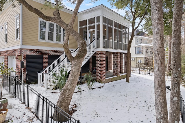 snow covered rear of property with a sunroom