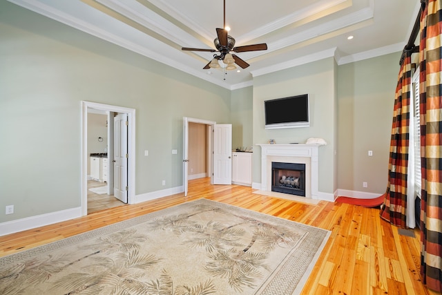 unfurnished living room featuring a raised ceiling, crown molding, ceiling fan, and light hardwood / wood-style flooring