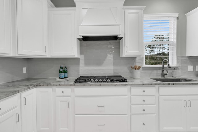 kitchen featuring white cabinetry, stainless steel gas stovetop, light stone countertops, sink, and custom range hood