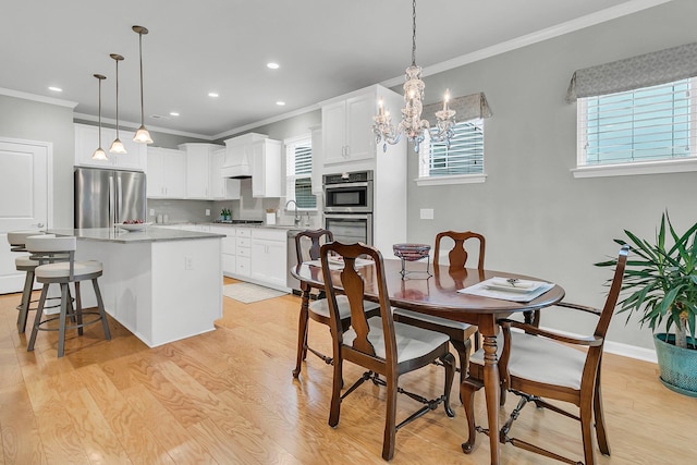 dining room featuring sink, ornamental molding, a notable chandelier, and light hardwood / wood-style flooring