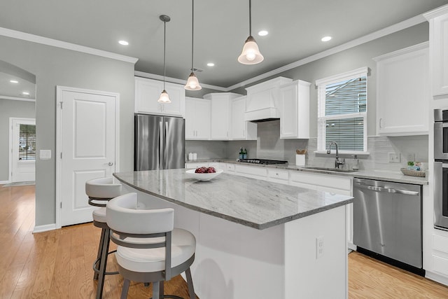 kitchen featuring appliances with stainless steel finishes, light stone counters, white cabinetry, a kitchen island, and crown molding