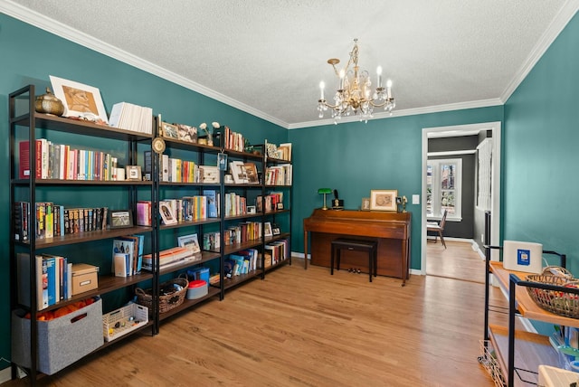 living area with wood finished floors, baseboards, ornamental molding, a textured ceiling, and a chandelier