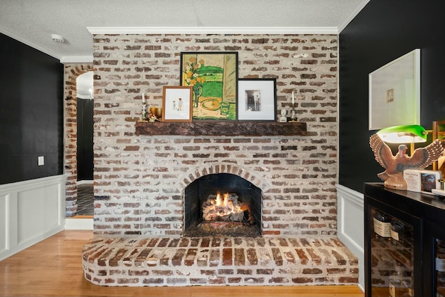 unfurnished living room featuring a textured ceiling, a brick fireplace, wainscoting, and ornamental molding