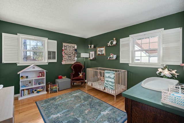 bedroom featuring a textured ceiling, a crib, and wood finished floors