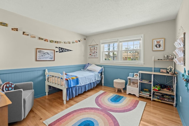 bedroom with a textured ceiling, wood finished floors, and wainscoting