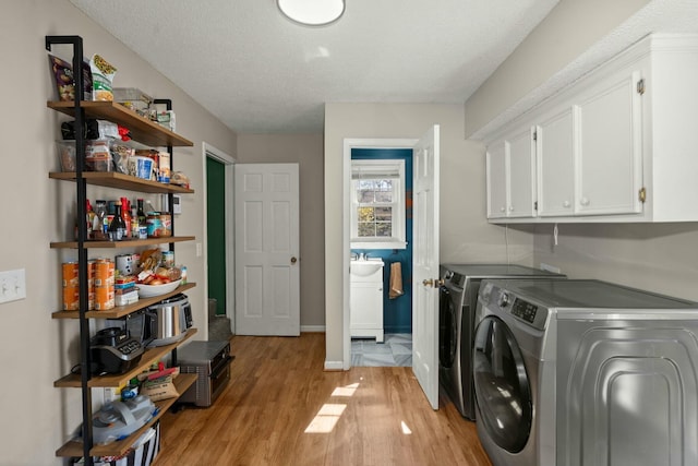 clothes washing area with independent washer and dryer, a textured ceiling, cabinet space, light wood finished floors, and baseboards