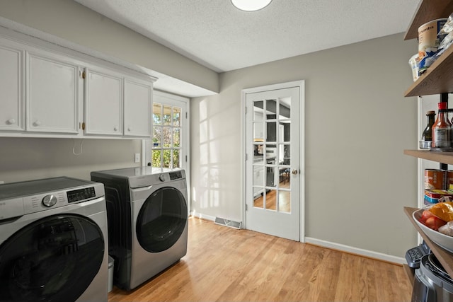 clothes washing area with visible vents, washing machine and dryer, light wood-type flooring, cabinet space, and a textured ceiling