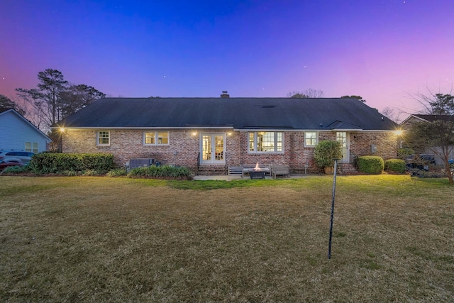 rear view of property with french doors, a yard, a chimney, and brick siding