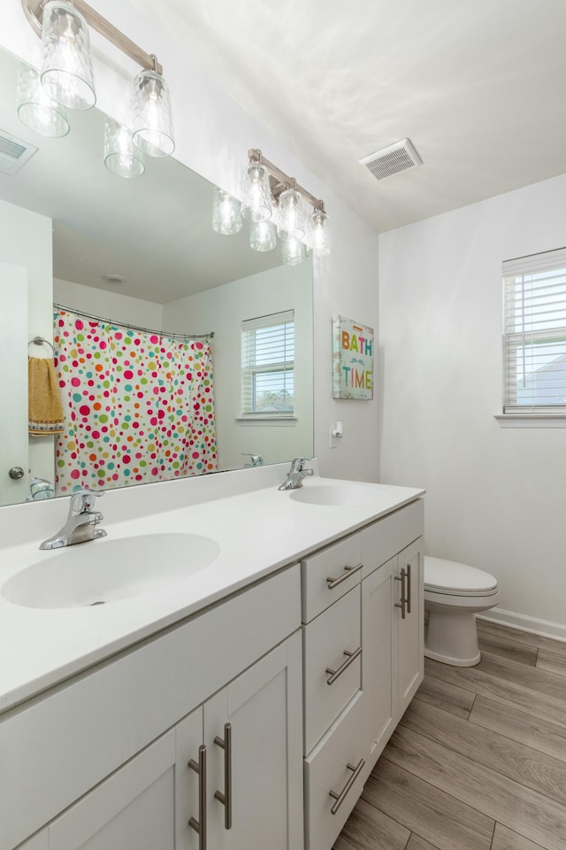 bathroom with toilet, wood finished floors, visible vents, and a sink