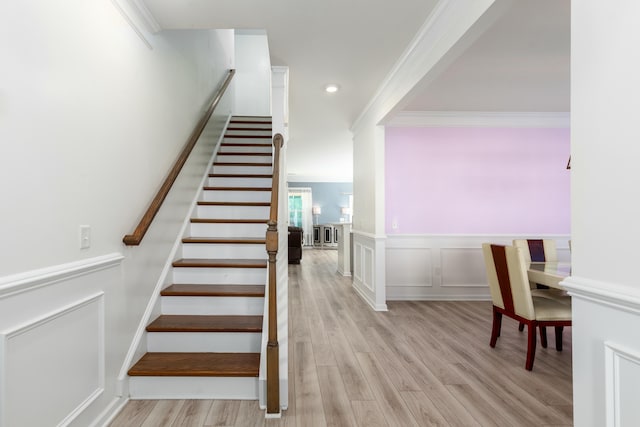 stairs featuring crown molding, a decorative wall, wood finished floors, and a wainscoted wall