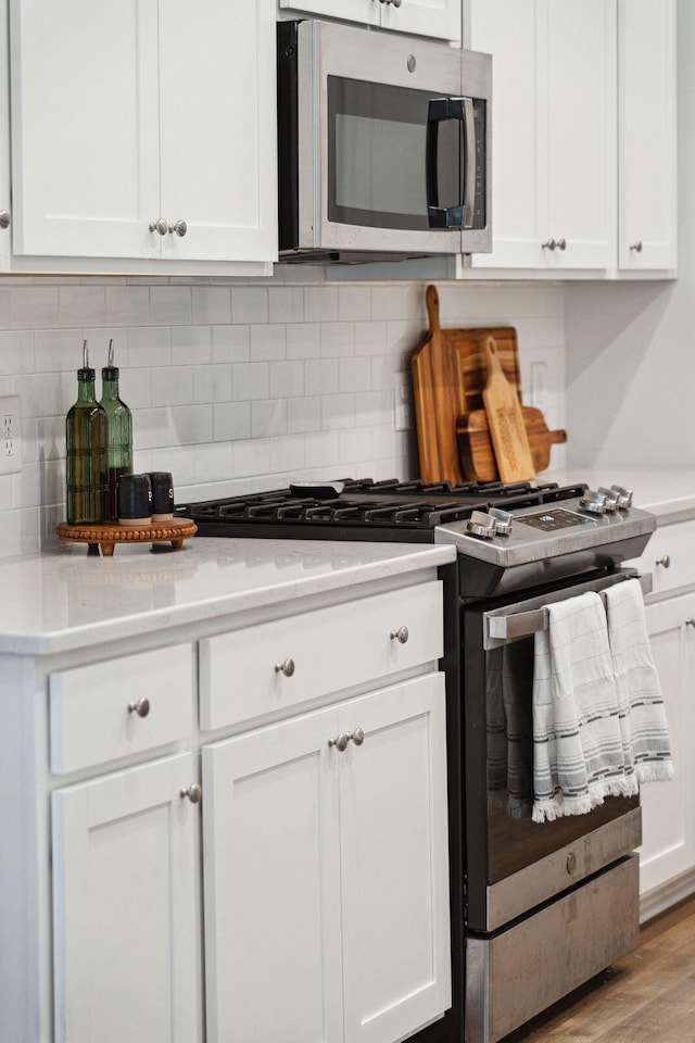 kitchen with decorative backsplash, stainless steel appliances, white cabinetry, and light hardwood / wood-style floors