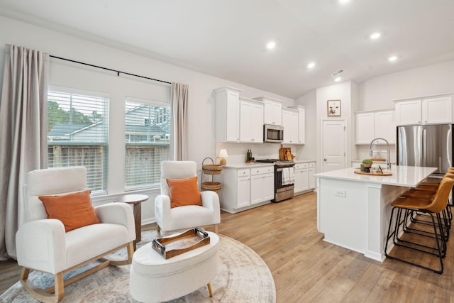 kitchen featuring white cabinets, a kitchen breakfast bar, an island with sink, appliances with stainless steel finishes, and light hardwood / wood-style floors