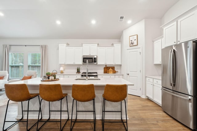 kitchen featuring white cabinets, appliances with stainless steel finishes, a breakfast bar, and a center island with sink