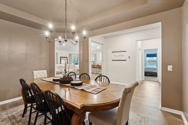 dining space with a notable chandelier, a raised ceiling, and light hardwood / wood-style flooring