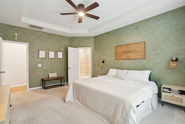 carpeted bedroom featuring a tray ceiling, ceiling fan, and ensuite bathroom