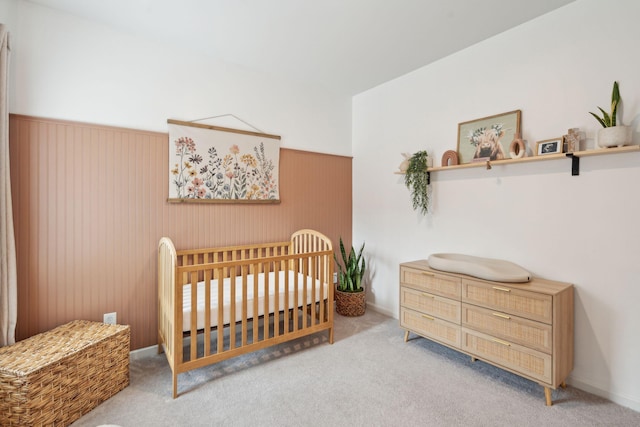 bedroom with a crib, light carpet, and wooden walls