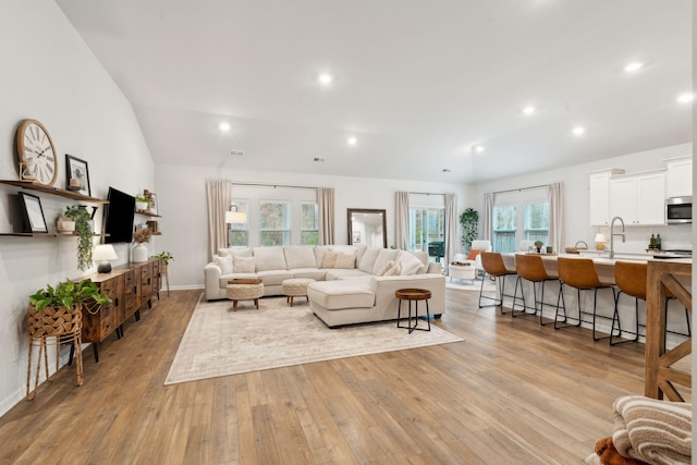 living room with vaulted ceiling, sink, and light hardwood / wood-style flooring