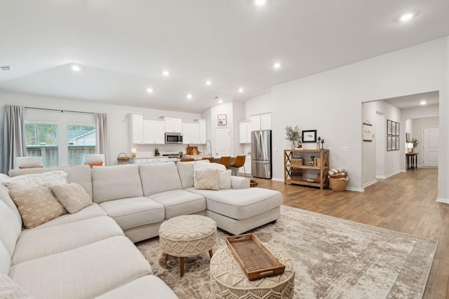 living room featuring sink, light hardwood / wood-style floors, and lofted ceiling