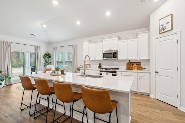 kitchen with appliances with stainless steel finishes, a kitchen breakfast bar, sink, lofted ceiling, and an island with sink