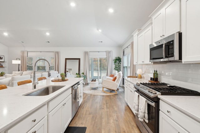 kitchen with lofted ceiling, backsplash, white cabinets, sink, and stainless steel appliances