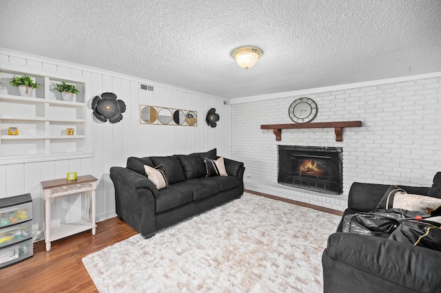 living room with a brick fireplace, brick wall, a textured ceiling, hardwood / wood-style floors, and wood walls