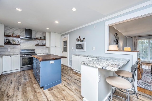 kitchen with tasteful backsplash, stainless steel range, white cabinets, and wall chimney range hood