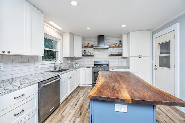 kitchen featuring white cabinets, wall chimney range hood, appliances with stainless steel finishes, butcher block countertops, and a kitchen island