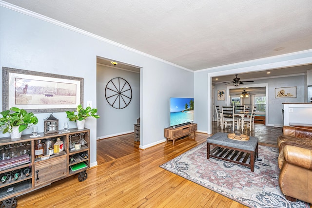 living room featuring crown molding, hardwood / wood-style floors, ceiling fan, and a textured ceiling