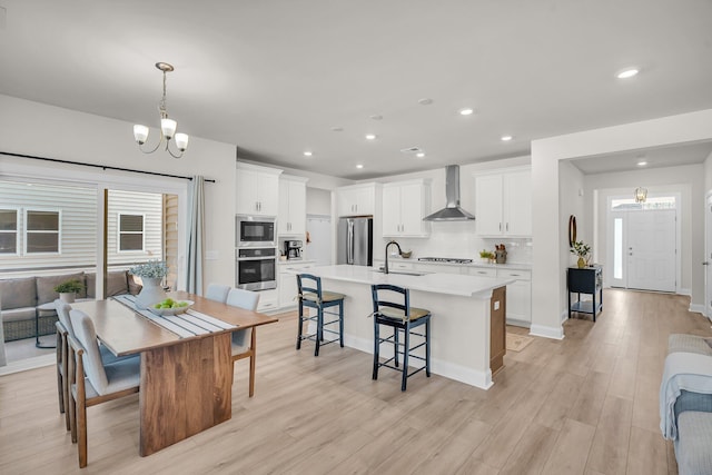 kitchen featuring white cabinetry, stainless steel appliances, decorative light fixtures, and wall chimney range hood