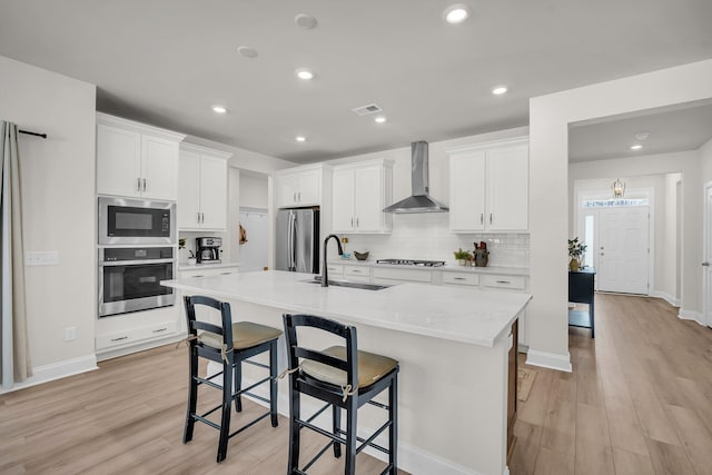 kitchen with sink, appliances with stainless steel finishes, white cabinetry, a kitchen bar, and wall chimney exhaust hood