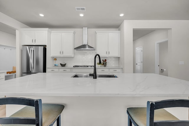 kitchen featuring wall chimney exhaust hood, sink, stainless steel refrigerator, light stone countertops, and white cabinets