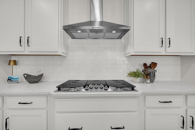 kitchen with stainless steel gas stovetop, light stone countertops, wall chimney range hood, and white cabinets