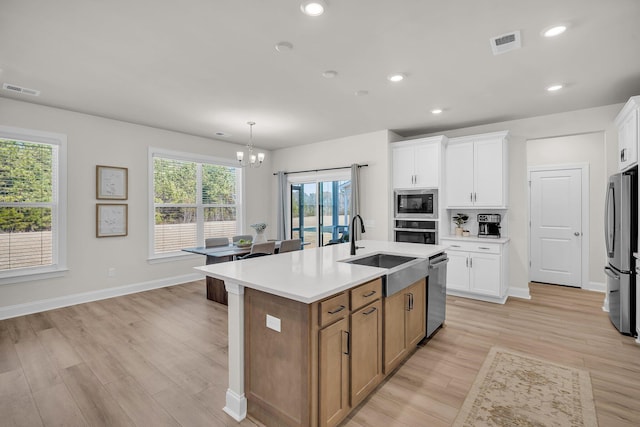 kitchen with hanging light fixtures, stainless steel appliances, an island with sink, and white cabinets