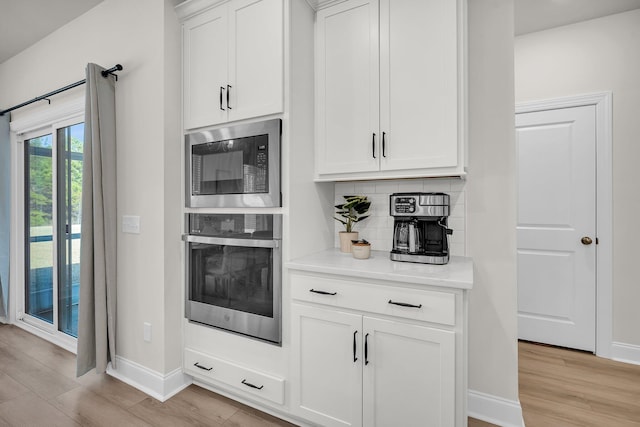 kitchen with white cabinetry, backsplash, built in microwave, oven, and light wood-type flooring